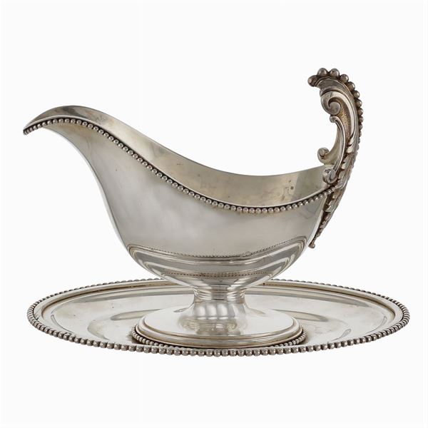 A silver sauce boat resting on an oval tray