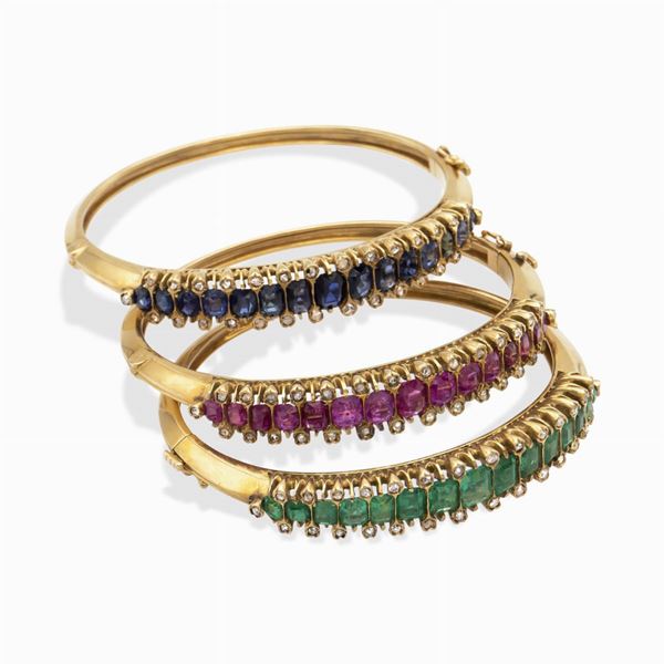 Tre bracciali a manetta in oro giallo 18kt con rubini, zaffiri e smeraldi